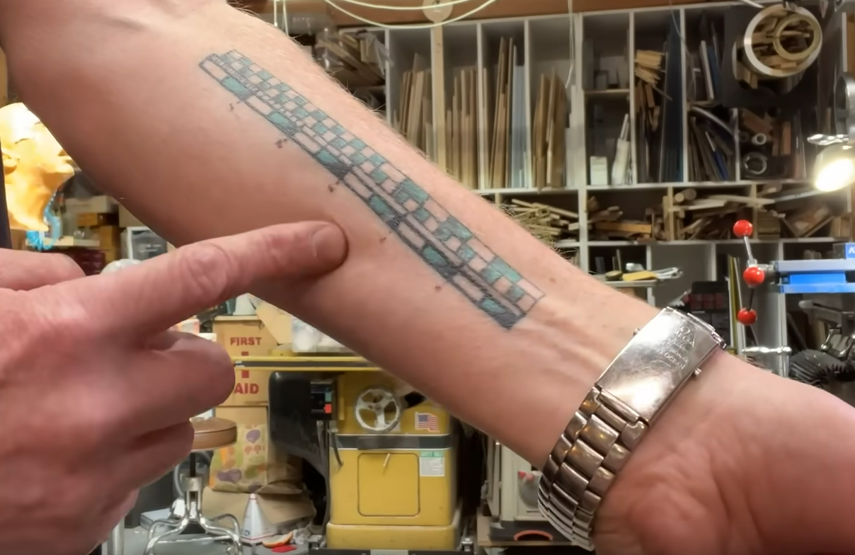 Adam Savage mostrando sua tatuagem de régua no antebraço